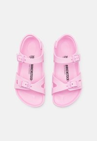 Pink plastic sandals with two adjustable buckles and multi-shaped cutouts. The footbed is textured for grip, featuring brand labeling on the insole.