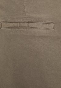 Close-up van beige stof met een horizontale paspelzak met nette stiksels en diagonale twillstructuur.