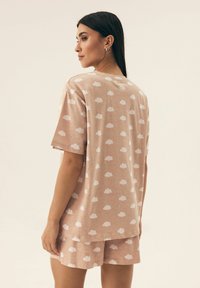 Jasnoróżowy zestaw odzieży domowej z bawełny, składający się z koszulki z krótkim rękawem i szortów z białym wzorem chmur. Miękka tekstura i luźny krój.