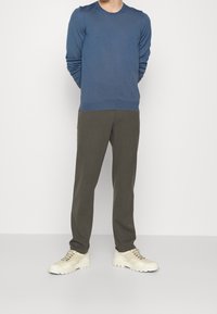 Modrý dlouhý rukáv svetr s kulatým výstřihem, zkombinovaný s olivově zelenými zúženými kalhotami a světle béžovými teniskami. Hladká tkanina s uvolněným střihem.