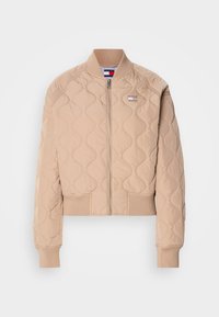 Paded bomber jakas šviesiai smėlio spalvos, su užtrauktuku priekyje, nuimtais rankogaliais ir apačioje, su logotipo apskritimu kairėje krūtinės pusėje.