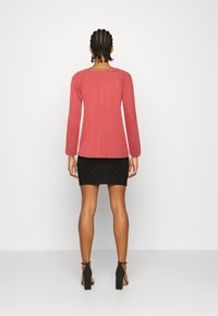 Blusa vermelha de manga longa com decote redondo, combinada com uma saia preta justa. O conjunto apresenta uma textura suave e um design simples.