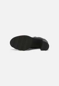 Semelle de chaussure à talon noir avec une surface en caoutchouc texturée. Elle comporte des rainures horizontales et un design à bout arrondi.