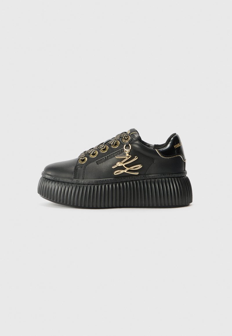 Svarta lädersneakers med en kraftig räfflad sula, guldfärgade detaljer, dekorativ snörningshardware och en logotypdetalj på sidan.