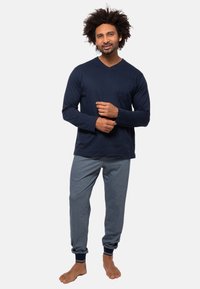 Marineblaues Langarm-V-Ausschnitt-Shirt mit einer Brusttasche, kombiniert mit grauen Jogginghosen mit Knöchelbündchen. Weicher Baumwollstoff, lässige Passform.
