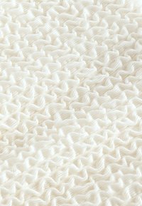 Teksturirana bela tkanina z izbočenim, gubanim vzorcem. Material je mehak, pleten in ima neprekinjen, valovit vzorec po vsej površini.