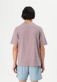 Short-sleeve, relaxed-fit t-shirt in light mauve cotton, featuring a crew neckline and stitched hem, worn with light blue shorts.