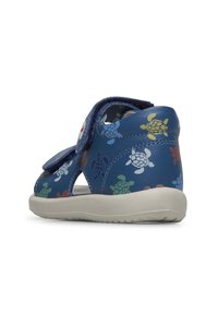 Blauwe leren schoen met open zijkanten, voorzien van kleurrijke schildpadprints. Inclusief een klittenbandsluiting en een lichtgekleurde rubberen zool.