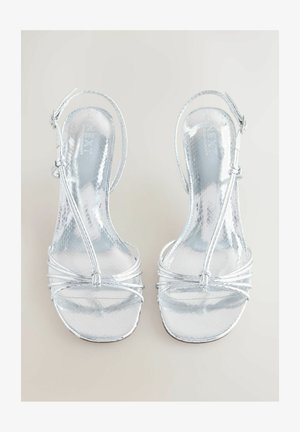 Silverfärgade högklackade sandaler med en glansig, strukturerad yta. Har tunna remmar och ankelsupport med knutdetaljer. Öppen tå-design.