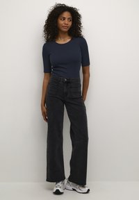 Haut bleu marine ajusté à manches courtes, jeans noirs taille haute à jambes larges, tissu texturé, quincaillerie argentée, associé à des baskets grises.