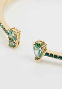 Gouden armband met twee peervormige groene edelstenen en een rij kleinere teal stenen, met een gladde, glanzende Oberfläche en een gestructureerd ontwerp.