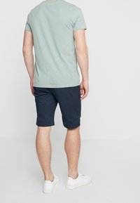 Ljusgrön kortärmad T-shirt, marinblå shorts. Blandning av bomullsmaterial, avslappnad passform, enkel design. Vita sneakers med minimala detaljer.