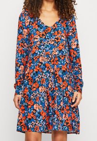 Květinové šaty s dlouhým rukávem a V výstřihem, s černým pozadím a živými vzory květin v oranžové, modré a růžové barvě. Detaily ve tvaru zvonku.