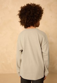 Helehall pikkade varrukatega särk, mis on valmistatud pehmest materjalist ja mille lõige on lõdvestunud, ümmarguse kaelusega ning langetatud õmblustega õlgadel.