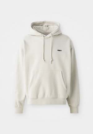 Beige Hoodie mit einer Vorderöffnungstasche, Kordelzug Kapuze und schwarzem "OBEY" Logo auf der linken Brust. Hergestellt aus weichem, strukturiertem Material.