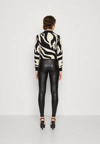 Svart och krämfärgad zebra-mönstrad tröja med åtsittande svarta faux läderleggings. Modellen bär högklackade sandaler, sedd bakifrån.