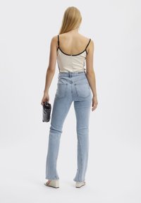 Top corto beige claro con bordes negros, combinado con jeans de mezclilla claros de talle alto y acampanados. La modelo sostiene un bolso negro.