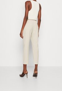 Beige beskurna byxor med elastisk midja, slät textur och avsmalnande ben, i kombination med bruna öppna klackar.