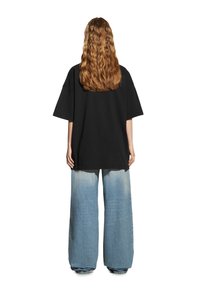 Czarna, oversize koszulka z bawełny, w połączeniu z szerokimi dżinsami w niebieskim kolorze, charakteryzującymi się wyblakłym odcieniem i luźnym krojem.