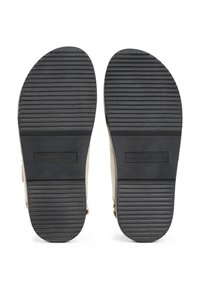 Semelles en caoutchouc noir avec des rainures horizontales sur des chaussures beiges, nom de marque "Tommy Hilfiger" embossé au centre de chaque semelle.