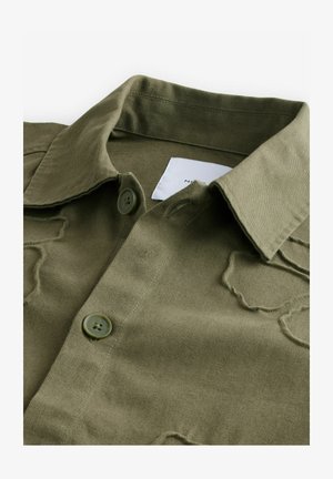 Olivgrünes Hemd mit Knopfleiste aus strukturiertem Stoff, punktiertem Kragen, zwei Brusttaschen und einem dezenten, abgetragenen Muster.