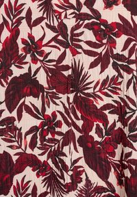 Patrón floral rojo y negro sobre una tela color crema claro, con varias formas de hojas y diseños de flores, y una superficie texturizada.