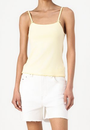 Slank person iført en bleg gul spaghetti-strop top og hvide højttaljede denimshorts med rå kant.