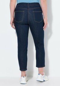 Tummansinisiä farkkuja, joissa on joustava vyötärö, kaksi takataskua ja lyhennetty suora lahje, yhdistettynä valkoisiin ja sinisiin lenkkareihin.