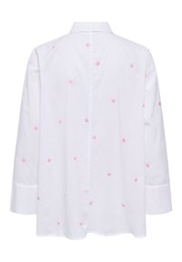 Chemise blanche à manches longues avec col, décorée de petits cœurs roses brodés dispersés sur le tissu.