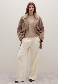 Brauner kariert übergroßer Mantel, beiger Pullover und weiße Hose mit weitem Bein. Glatte Texturen, kontrastreiche Farben und strukturierte Formen.