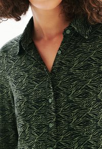 Chemise vert à boutons avec un motif de rayures zebra noir et vert, en coton, et un design de col classique avec des boutons assortis.