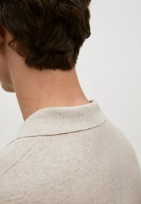 Polo beige avec un tissu texturé et un col doux, montré de dos, mettant en avant la zone du cou et les détails de la chemise.