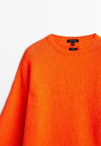Pull en tricot orange avec un col rond et une coupe ample. La texture semble douce et duveteuse, arborant une couleur uniforme et vive.