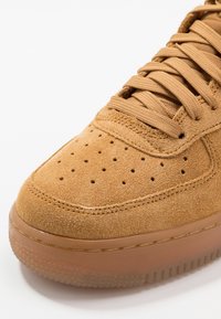 Tan mockasinsneaker med perforerad tåbox, platta snörningar och semi-genomskinlig gummisula. Rundad form med sömnadsdetaljer.