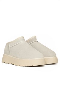 Zapatos mocasines de ante beige con una suela gruesa crema, puntera redondeada y un detalle de costura mínima en la parte superior. Textura suave en todo.