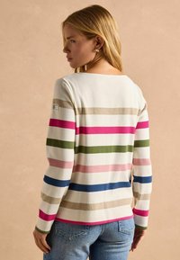 Balts garās piedurknes tops ar horizontālām svītrām rozā, zaļā, zilā un bēšā krāsā. Ievērojamas noapaļotas kakla līnijas un mīksta, teksturēta auduma.