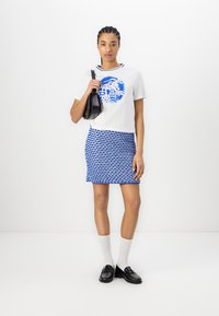 Hvid t-shirt med blåt grafisk design, parret med en blå mønstret miniskørt. Sort håndtaske og loafers, med hvide sokker.