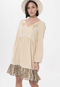 Beige lange mouw jurk met een V-hals, bloemenborduurwerk, kanten rand en een gerimpelde slangenprint onderzoom. Lichtgewicht stof.