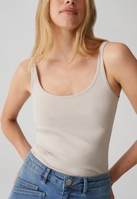 Beiges Stretch-Top mit U-Ausschnitt aus weichem Stoff, kombiniert mit blauen, hoch Taillen Jeans aus Denim. Keine sichtbaren Muster oder Verzierungen.