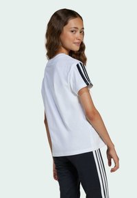 White cotton t-shirt featuring black horizontal stripes on the sleeves and a relaxed fit, paired with black pants with white side stripes.