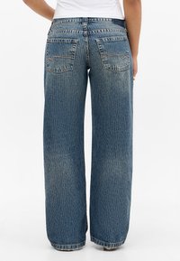 Bredbens denimjeans i blå med lodrette ribber har to baglommer og en let frynset kant ved anklerne, lavet af tekstureret bomuldsstof.
