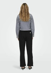 Jachetă din denim gri, scurtă, cu mâneci lungi și închidere cu nasturi, asortată cu pantaloni negri cu picioare largi. Design minimalist, croială ajustată.