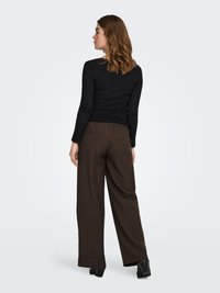 Black long-sleeve top with a ribbed texture, paired with high-waisted, wide-leg brown trousers. The outfit features minimal design accents.