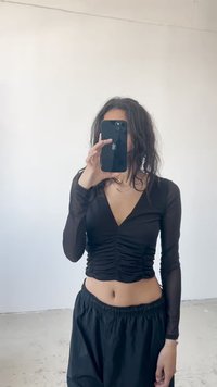 Schwarz langärmliges Oberteil mit V-Ausschnitt und Raffung an der Vorderseite, kombiniert mit schwarzen lockeren Hosen. Glattes, semi-transparentes Material.