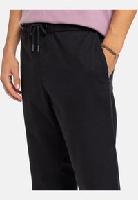 Čierne pohodlné nohavice s elastickým pásom a detailom na sťahovanie. Tkanina sa zdá byť hladká; má bočné vrecká a jemné prešitie.