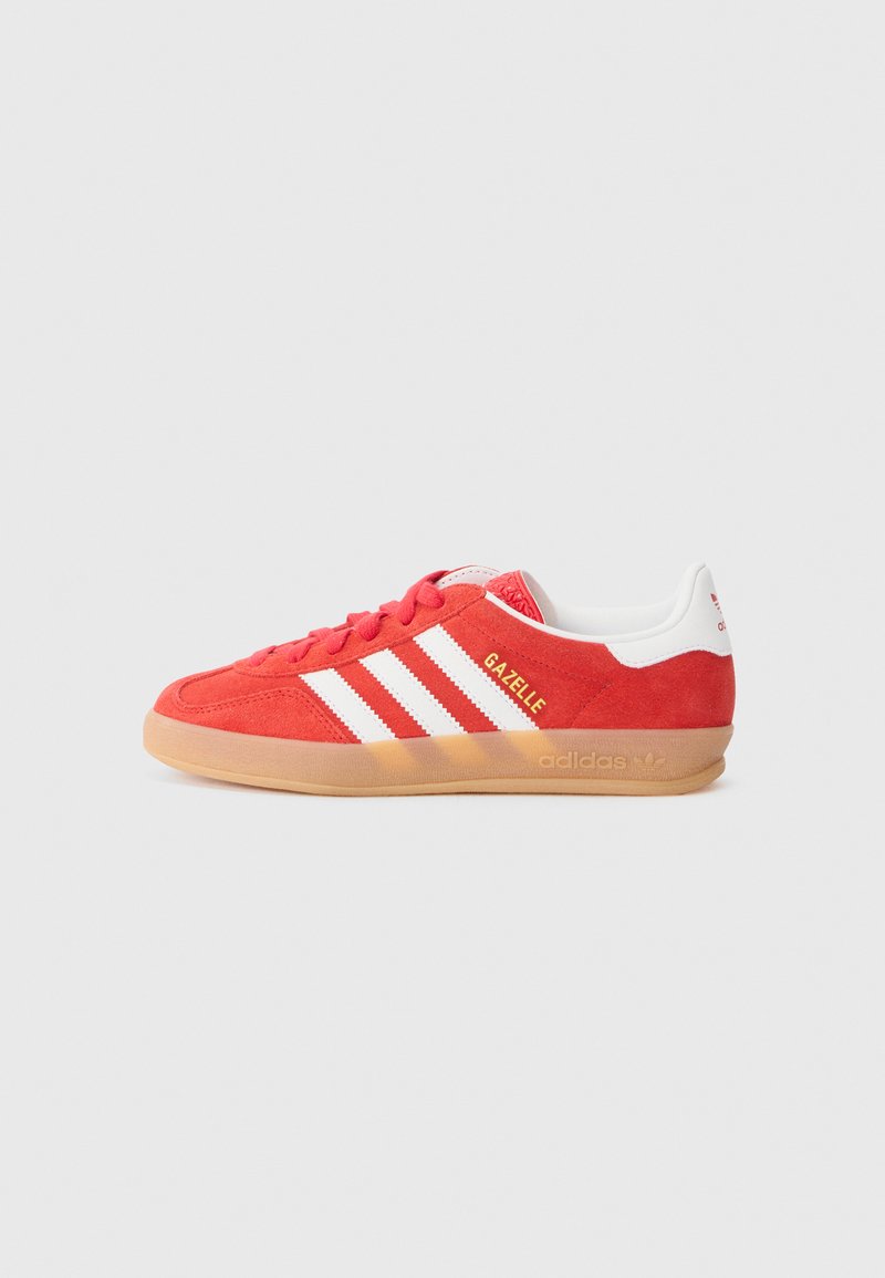 Röd mocka sneakers med vita tre ränder, gummisulor och gyllene "Gazelle"-text. Låg profil, rund tå och snörning framtill.