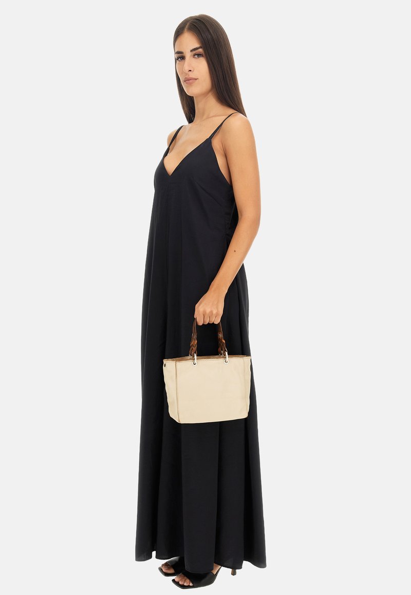Borsa beige con manici intrecciati marroni, forma rettangolare, dettagli cuciti, tenuta da un modello in un abito maxi senza maniche nero.
