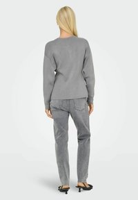 Grå tröja med en avslappnad passform, långa ärmar och rund halsringning, i kombination med högmidjade grå jeans och svarta klacksandaler.
