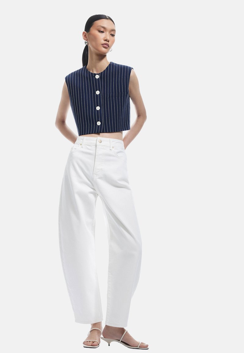 Marine gestreept cropped top met knoopsluiting, gecombineerd met witte wijde broek. Model draagt lichte, gespsandalen.
