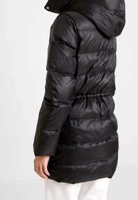 Chaqueta acolchada negra con capucha, que cuenta con un acabado texturizado y brillante, y secciones acolchadas horizontales. Diseñada para ofrecer calidez y comodidad.